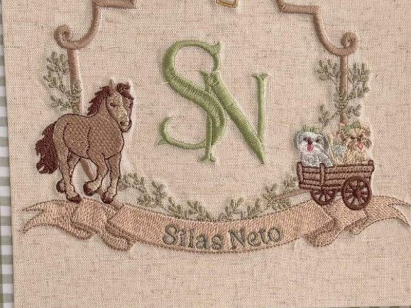 O p�nei bordado � esquerda e a carrocinha de madeira com dois animaizinhos � direita, sobre a faixa do nome