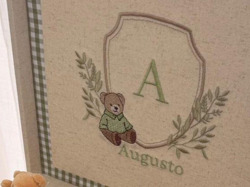 Escudo bordado com a letra A em verde, ramos de oliveira, ursinho de camisa verde sentado e o nome Augusto bordado embaixo