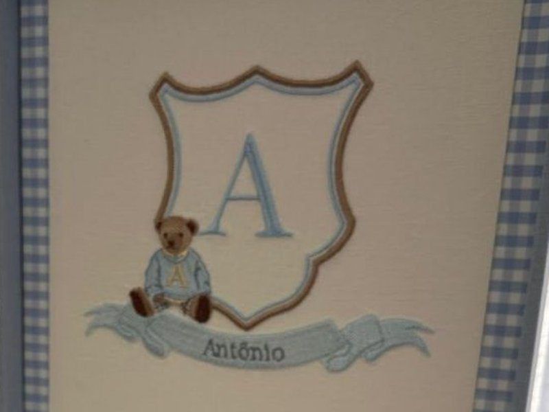 Escudo bordado com a letra A, ursinho de su�ter azul sentado e faixa com o nome Ant�nio